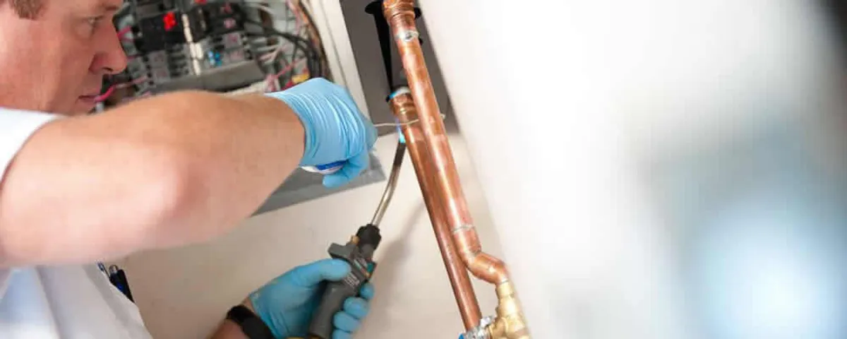 Water heater repair technician testing copper pipe connections and controls in Mesa, AZ